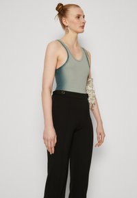 Svetle tyrkysový bodysuit s hlubokým výstřihem, kombinovaný s černými kalhotami s vysokým pasem, které mají boční akcent a stříbrnou třásňovou tašku.