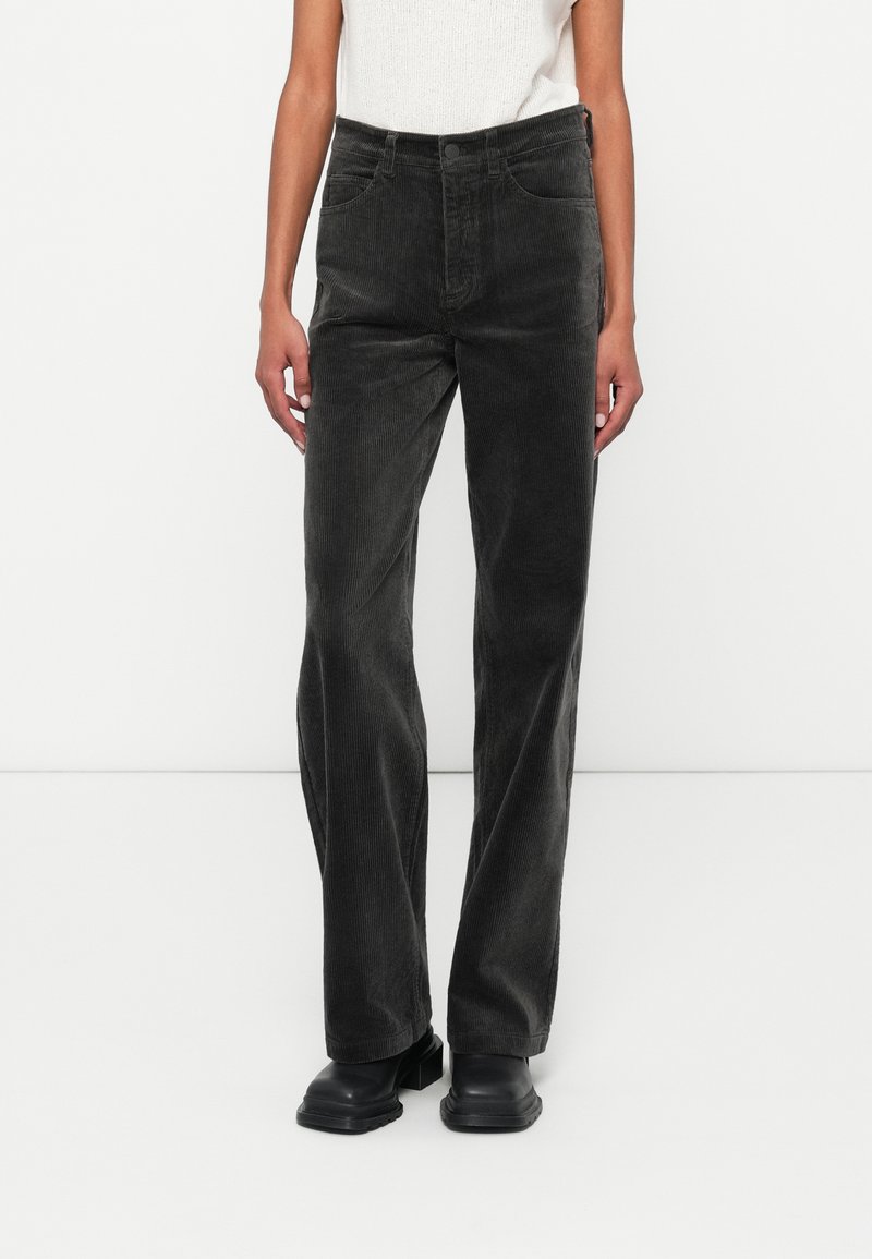 Pantalon en velours côtelé noir avec une coupe droite, présentant des poches avant et une surface légèrement texturée, associé à des chaussures noires.