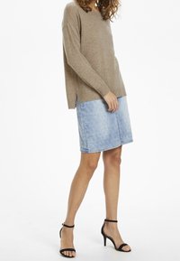 Beżowy sweter z dzianiny o prążkowanej fakturze i bocznych rozcięciach, zestawiony z jasnoniebieską spódnicą jeansową z delikatnym wzorem oraz czarnymi sandałami na paski.