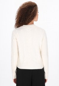 Kermainen kaulussyöttö neulepaita, jossa on pitkät hihat ja pyöreä kaula-aukko, jossa on tekstuurisia kuvioita ja tiukka vyötärö.