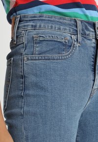 Jeans de mezclilla azul claro con un diseño ajustado, que cuentan con cinco bolsillos, costuras sutiles y un parche de cuero en la cintura trasera.