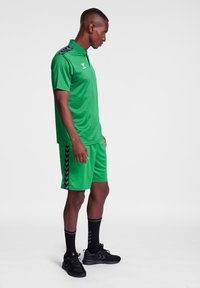 Grøn atletisk polo og shorts sæt lavet af letvægtsmateriale. Har sorte chevron detaljer på shortsene og et standard kravedesign.