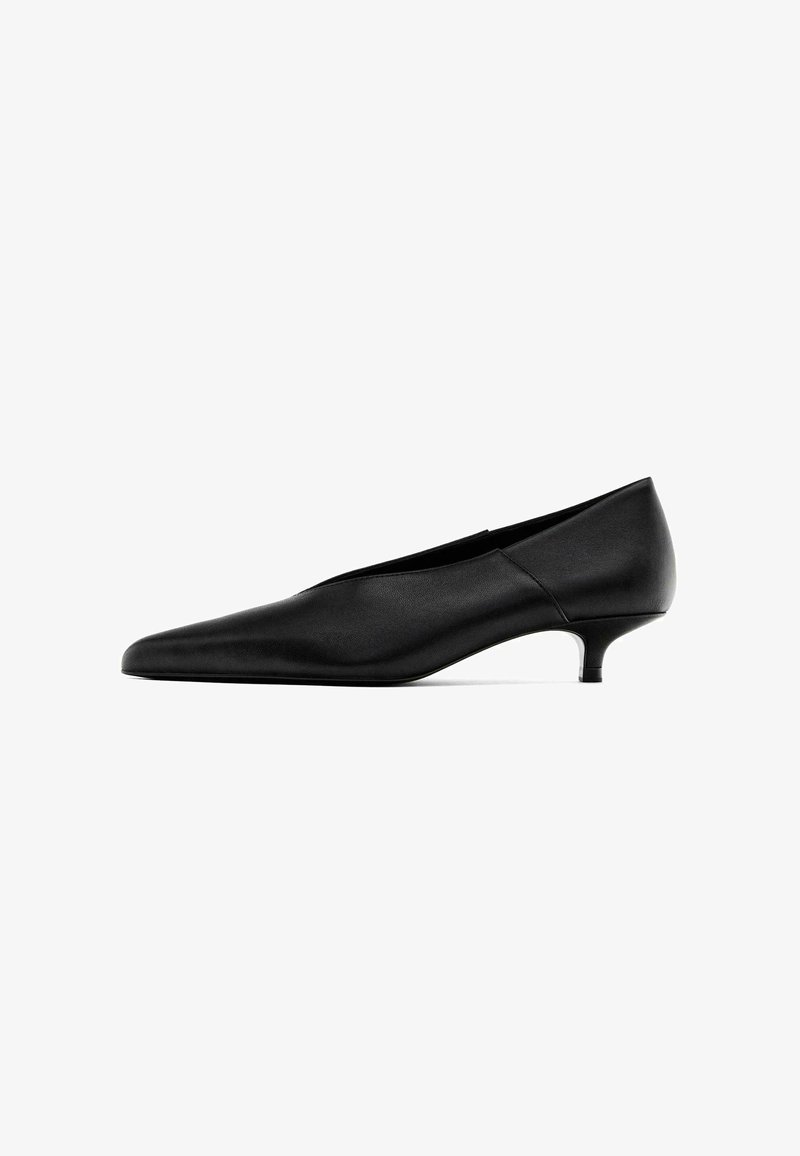 Chaussure en cuir noire à petit talon aiguille avec bout pointu et talon bas et fin, présentée sur fond blanc.
