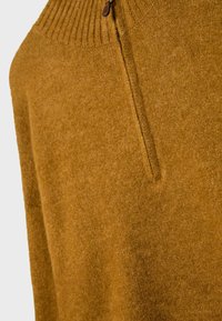 Gros plan sur un pull en laine couleur moutarde avec un col côtelé et une courte fermeture éclair marron au niveau de l'encolure.