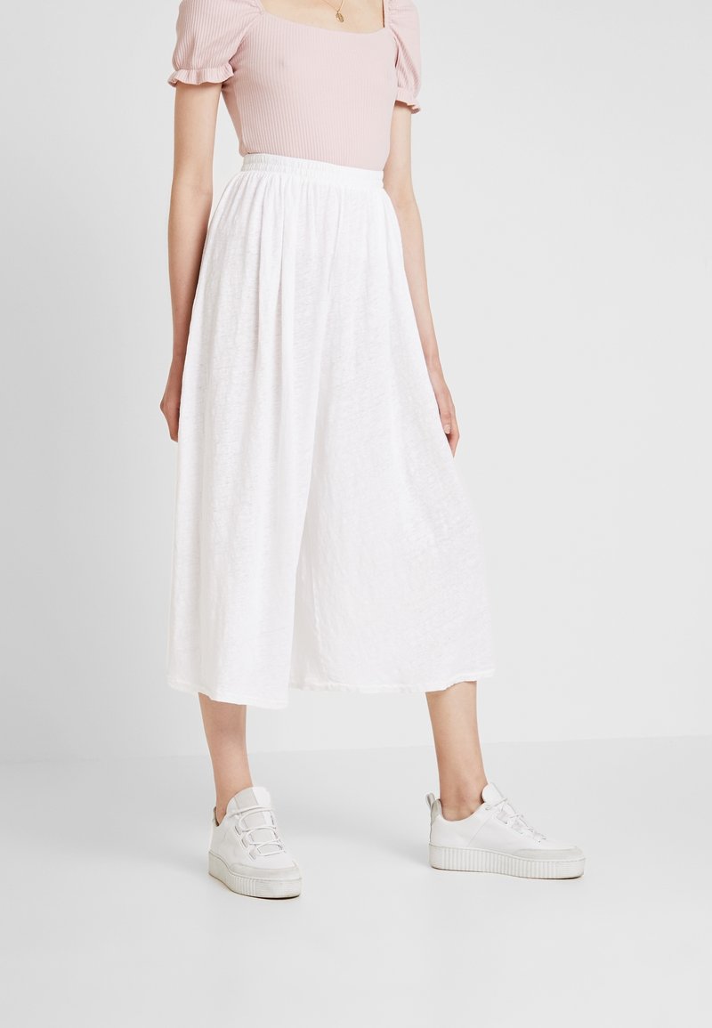 Vit, luftig kjol i midjelängd med texturerat tyg. Kombinerad med en ljusrosa figurnära topp och vita sneakers med texturerad sula.