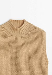 Pull sans manches beige en tricot avec un col montant côtelé épais et un motif de points texturé sur le corps.