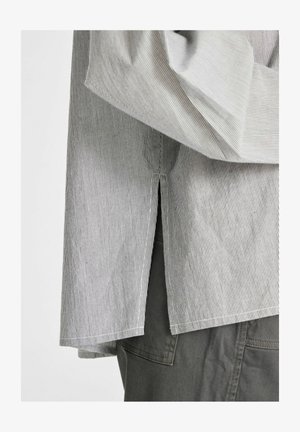 Pruhovaný sveter s voľným strihom, s vertikálnymi bielymi a šedými pruhmi, so bočným rozparkom a manžetami, skombinovaný s tmavošedými nohavicami.