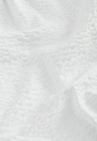 Tissu blanc texturé avec un motif doux en forme de gaufre et des plis subtils créant de légères ombres à la surface.