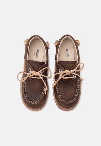 Paire de chaussures marron en cuir style mocassin avec lacets beiges, coutures visibles et branding Moschino Milano à l’intérieur.