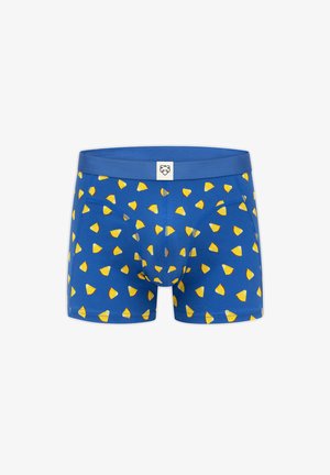 Mėlyni bokseriai su geltonos spalvos trikampių vaisių skiltelių raštu ir mažu baltu etikete, kurioje ant juostos vaizduojama stilizuoto gyvūno veidas.