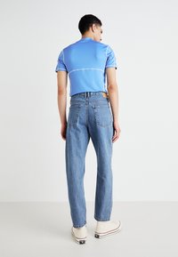 Blue fitted shirt with white stitching, paired with light blue straight-leg jeans and white high-top sneakers, viewed from the back.
