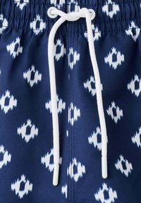 Tissu bleu marine avec des motifs géométriques blancs et un cordon blanc enfilé dans des œillets métalliques à une taille élastique.