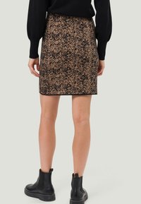 Jupe noire et à motifs avec une coupe ajustée, dotée d'un tissu texturé et d'un ourlet droit, associée à des bottines noires.