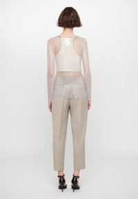 Gjennomsiktig mesh langermet topp i sølv med nøkkelhullsdetalj bak, kombinert med beige skreddersydde bukser og svarte hælsandaler.