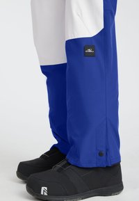 Blue and white snow pants with O'Neill logo over black snow boots on a white background.