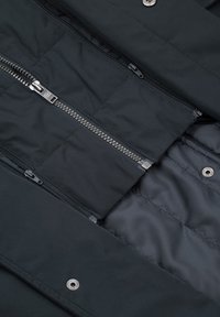 Czarna, pikowana kurtka z wieloma suwakami i srebrnymi okuciami. Gładka, matowa faktura tkaniny, z detalami na zatrzaski z przodu.