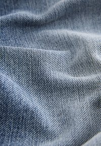 Záber zblízka na pokrčenú modrú denimovú látku ukazujúcu detailnú štruktúru tkania a diagonálne vzory.