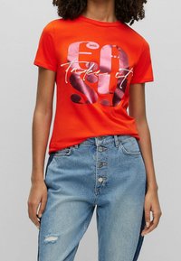 Czerwona bawełniana koszulka z dużym nadrukiem w odcieniach różu z napisem „Take it 40”, z okrągłym dekoltem i krótkimi rękawami. W zestawie z dżinsowymi spodniami.