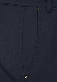 Pantalon en tissu bleu marine avec une texture lisse ; comporte une seule poche avec un bouton argenté et des détails de couture soignés.