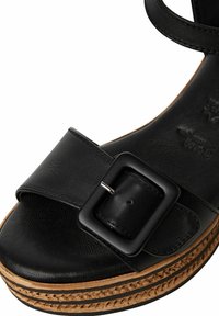 Černé kožené sandály se širokým popruhem, černou čtvercovou sponou a tkanou jutovou platformou. Hladký povrch s mírným leskem.