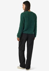 Zeleni puhasti pulover z zaobljenim izrezom, dolgimi rokavi in sproščenim krojem. Usklajen z črnimi širokimi jeans hlačami in sproščenimi čevlji.
