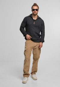 Mørkegrå strikket pullover med halvlukning og ribbet tekstur, parret med lysebrune corduroy cargo bukser og hvide sneakers.