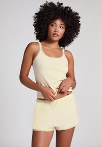 Geel geribbeld tanktop met kantafwerking, gecombineerd met bijpassende shorts met geschulpte randen en een kleine strikaccent bij de taille.