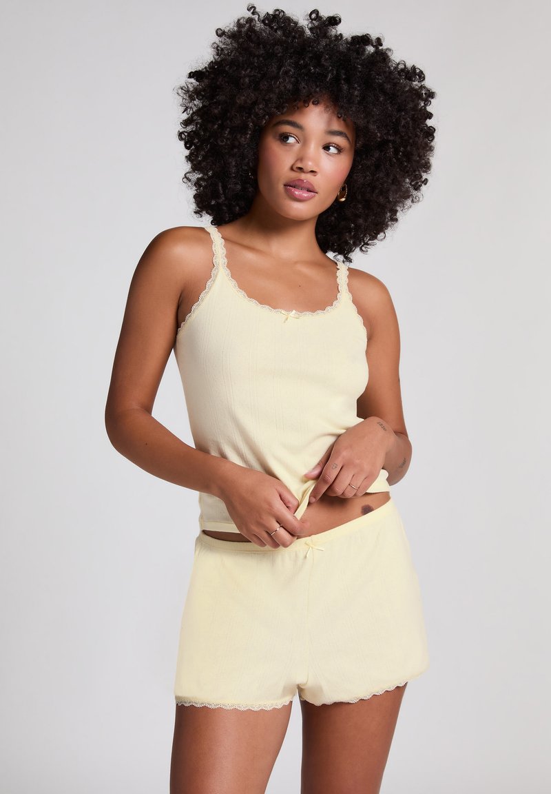 Geel geribbeld tanktop met kantafwerking, gecombineerd met bijpassende shorts met geschulpte randen en een kleine strikaccent bij de taille.