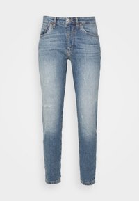 Vaqueros de mezclilla azul claro con un corte slim, con parches descoloridos, detalles desgastados, cinco bolsillos y cierre frontal con botón.