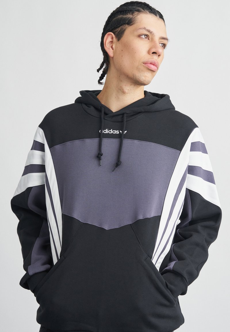 Čierna a sivá mikina s kapucňou s fialovým panelom na hrudi, bielymi pruhmi na rukávoch, nastaviteľnými šnúrkami a klokanie vrecko.