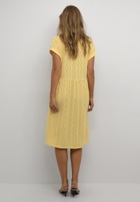 Kleid aus Augenstoff in Gelb, knielang, mit kurzen Ärmeln und tailliertem Schnitt, das ein wellenförmiges Muster und einen ausgestellten Rock hat.