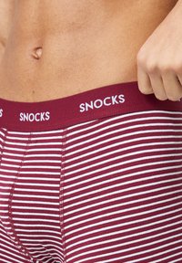 Pantalones cortos de boxeo a rayas marrón y blanco con una cinturilla sólida en marrón que presenta el logo "SNOCKS" en blanco. Material de algodón, diseño ajustado.