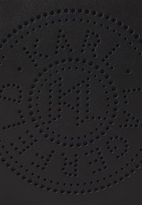 Czarny produkt ze skóry z ażurowym, okrągłym wzorem i centralnym logo. Gładka faktura i minimalistyczne detale metalowe podkreślają design.