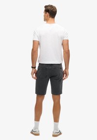 Shorts en denim gris à coupe droite, avec des coutures visibles et deux poches arrières. Associés à un t-shirt blanc uni et des chaussettes blanches.