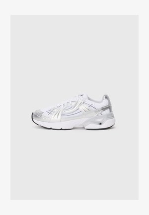 Zapatilla deportiva blanca con acentos plateados y paneles de malla. Punta redondeada, diseño con cordones y una suela gruesa con huella negra.