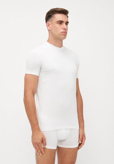 Weißes, kurzärmeliges, eng anliegendes T-Shirt aus glattem, elastischem Stoff, kombiniert mit weißen Boxer-Shorts, die ein nahtloses Design und klare Linien zeigen.