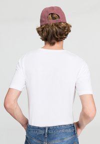 T-shirt bianco a maniche corte in cotone, abbinato a un cappellino da baseball color rosa polveroso. Il cappellino ha una fibbia regolabile e cuciture visibili.