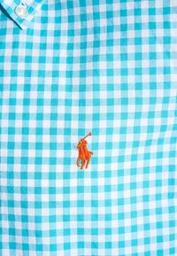 Ljusblå och vit rutig skjorta i bomull, med en liten orange broderad polo-spelare logotyp på vänster bröst.