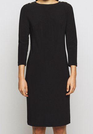 Woman wearing a fitted black knee-length dress with three-quarter sleeves and gold buttons on the shoulder seams.