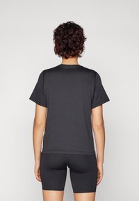 Czarny t-shirt z krótkim rękawem wykonany z gładkiej tkaniny, z klasycznym okrągłym dekoltem i luźnym krojem, zestawiony z czarnymi szortami rowerowymi.