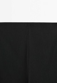 Gros plan sur un tissu noir avec une couture verticale centrale, montrant la texture et les détails subtils des points sur un fond blanc uni.