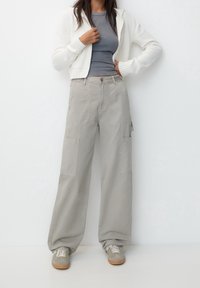 Pantaloni cargo grigi con gambe ampie, numerose tasche a toppa e materiale in cotone morbido, abbinati a un top grigio aderente e a una leggera felpa.