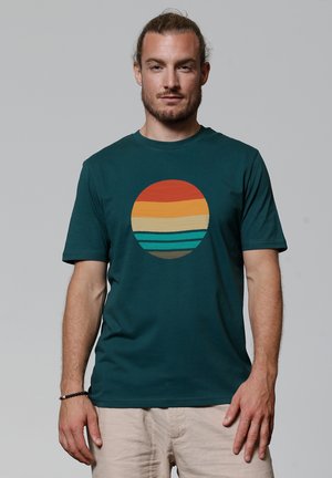 Teal katoenen t-shirt met een circulaire grafiek met oranje, gele en teal horizontale strepen. Crew neck ontwerp en korte mouwen.