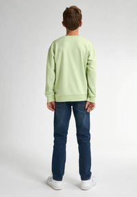 Lichtgroene sweatshirt met verlaagde schouders, ribbelboorden en -zoom, gecombineerd met donkerblauwe jeans en witte sneakers, gezien van achteren.