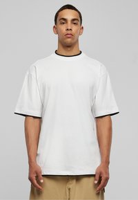 Vit t-shirt med kort ärm och svart kant vid halsen och ärmarna, med en avslappnad passform och mjuk bomullstextur.
