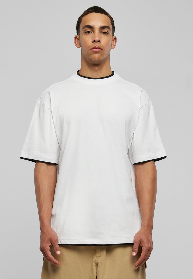 Vit t-shirt med kort ärm och svart kant vid halsen och ärmarna, med en avslappnad passform och mjuk bomullstextur.