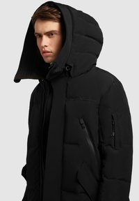 Juoda pūkinė striukė su dideliu gobtuvu, su siuvinėta tekstūra, kišenėmis su užtrauktukais ir lygiu paviršiumi. Savybė – elegantiškas, modernus dizainas.