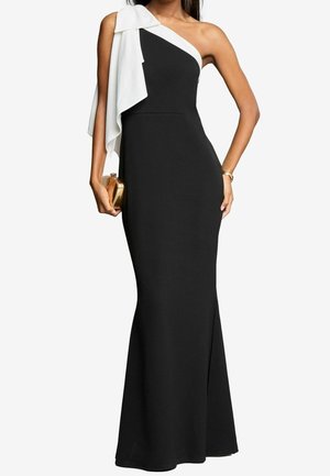 Czarna wieczorowa suknia z asymetrycznym, jedno-ramiennym fasonem, ozdobiona białą nakładką z tkaniny. Materiał jest gładki i dopasowany, z rozszerzanym dołem.