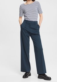Pantalones de pierna ancha en navy con cintura alta, que presentan pliegues y una textura suave, combinados con una blusa ajustada de rayas blancas y navy.