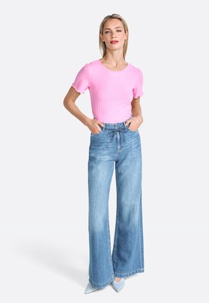 Haut rose clair à manches courtes côtelé associé à un jean taille haute à jambes larges bleu clair et des escarpins bleus à bout pointu. Design simple, coupe décontractée.